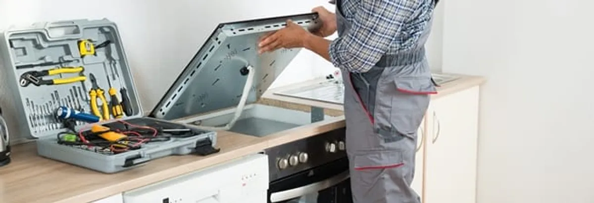 Cooktop repair technician lifting a built-in stovetop for service in Cleveland, OH